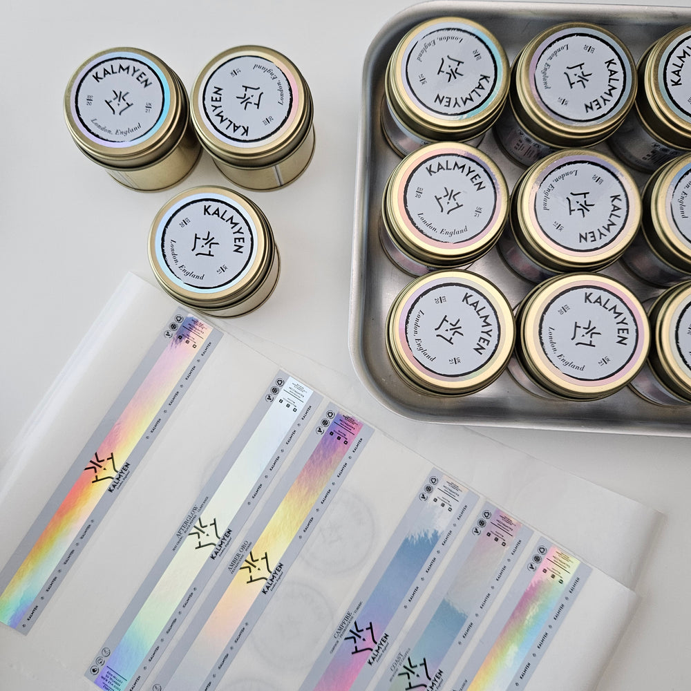 Kalmyen Keepsake tins arranged in a tray, being labeled with iridescent labels. The image showcases the process of adding the signature labels to the tins, adding a touch of elegance to the final product.