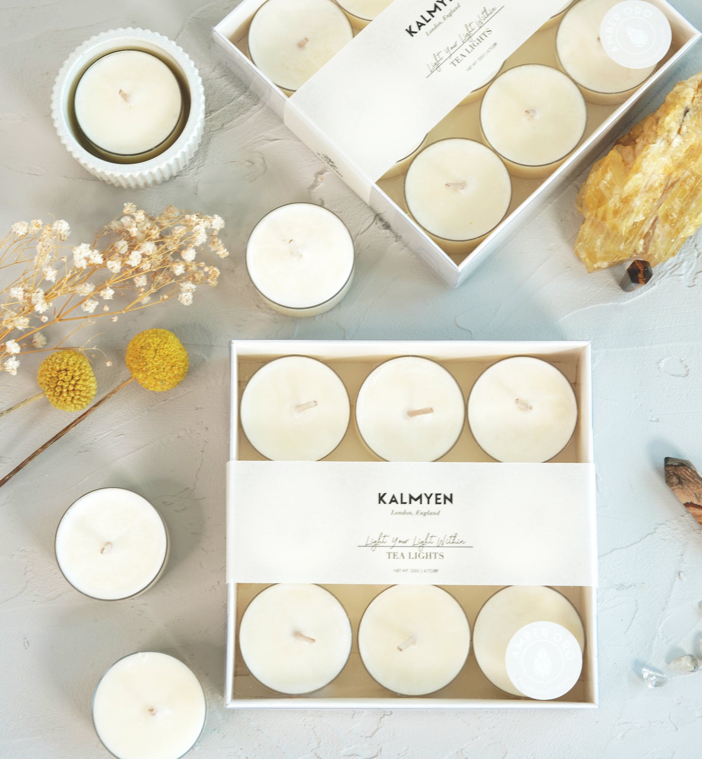 Image of amber oro tealight boxes with loose tealights and natural flowers in the background, accompanied by a large crystal and mini point tigers crystal.