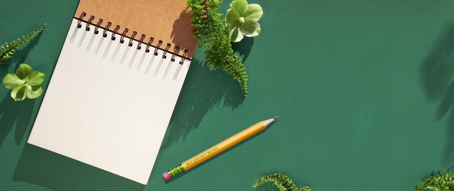 image showing a open notepad with pencil next to it on green background with some green decorative plants around it