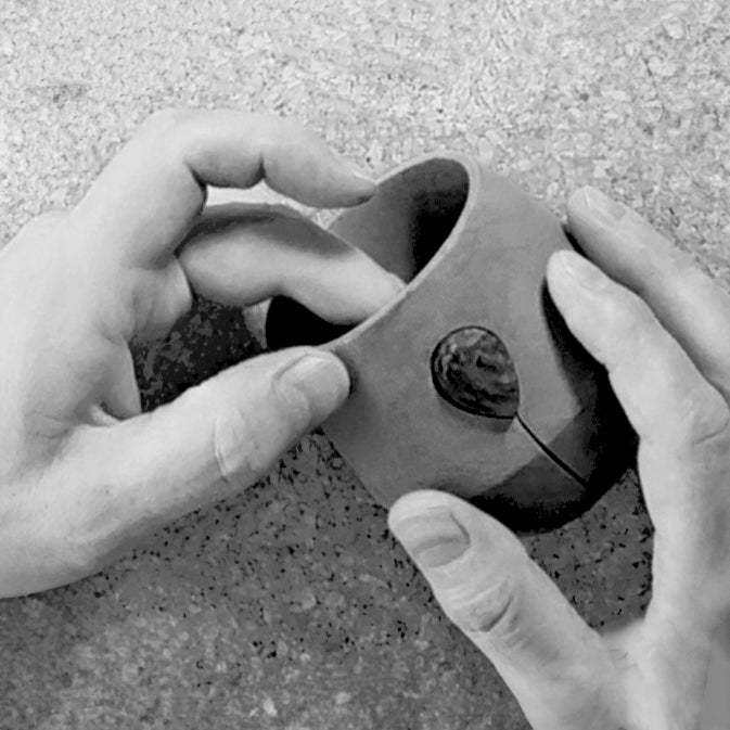 Kalmyen Luna jar being adorned with its gemstone crystal by hand, depicted in black and white.