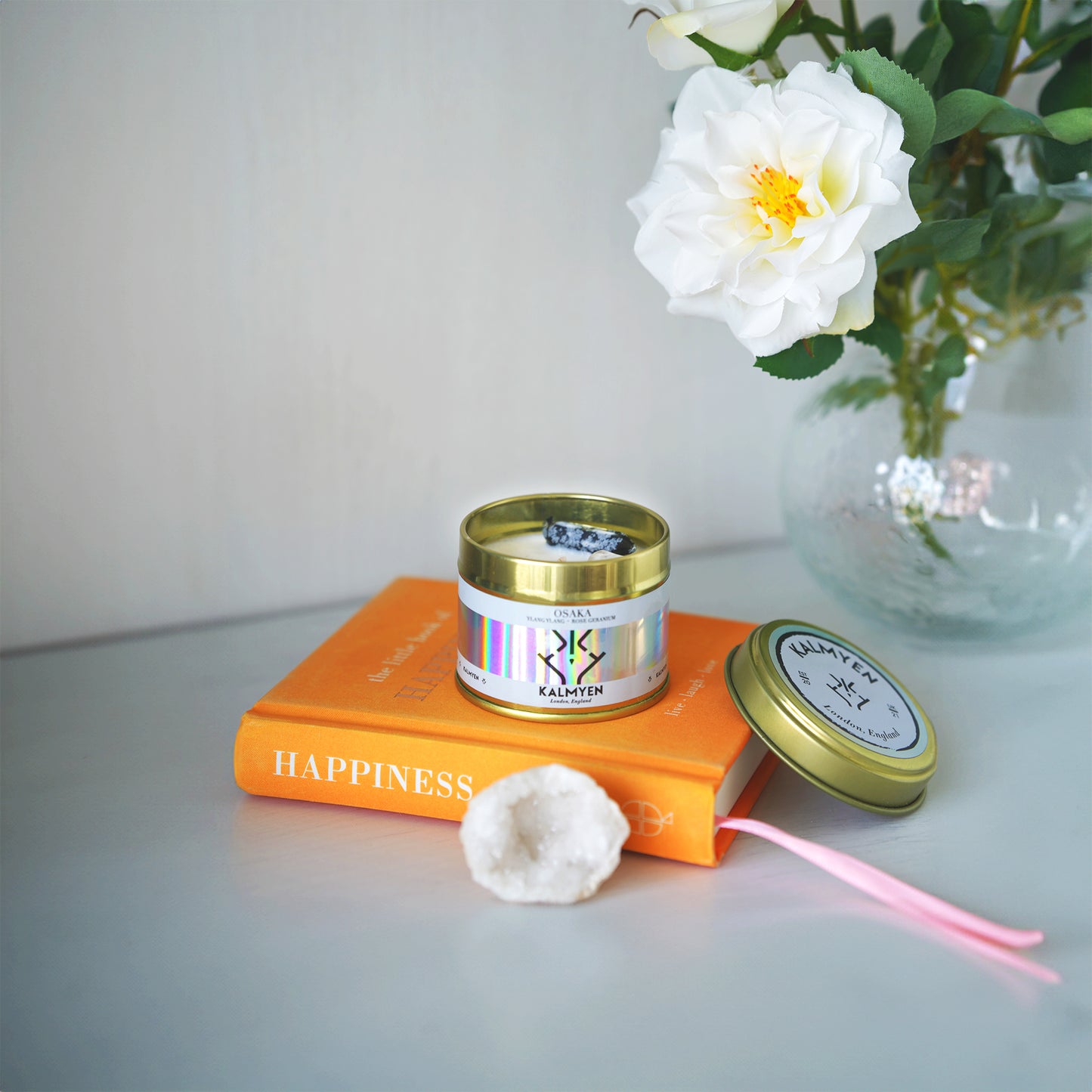 Osaka keepsake candle on shelf with 'Happiness' book and vase with white flower.