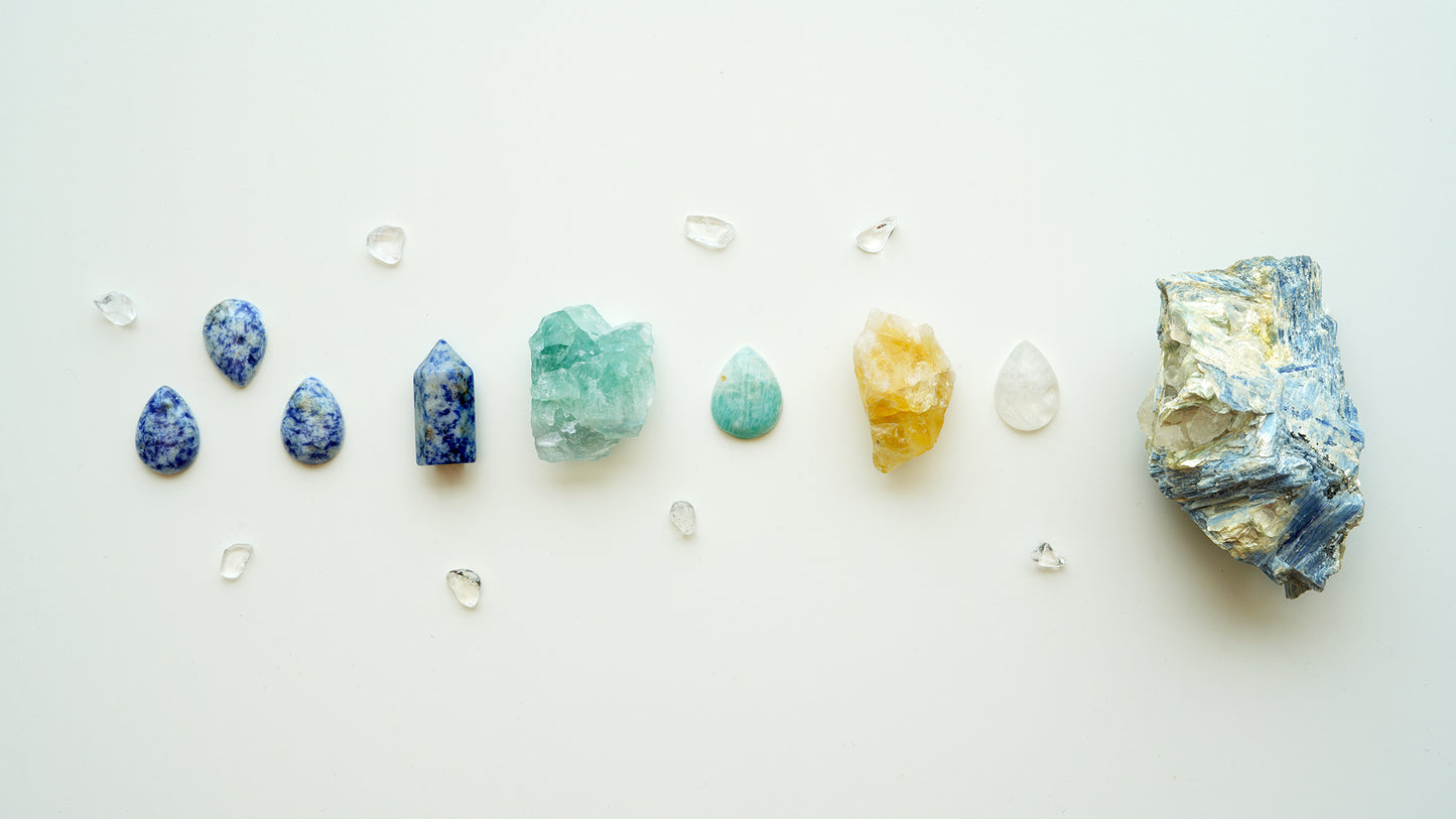 Line of crystals from raw to polished: Blue spot jasper tear drops, mini point, and amazonite nugget; tear drop shaped amazonite crystal; citrine nugget and clear quartz tear drop; celestite rock on the right side. Mini tumbled stones of clear quartz scattered throughout.