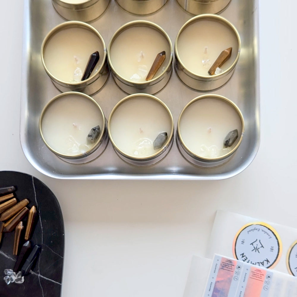 Top-down view of Kalmyen Keepsake tins, including Coast and Amber Oro variants, each embedded with labradorite and tiger's eye crystal gemstones. The arrangement showcases the exquisite craftsmanship and crystal adornments of the candles.