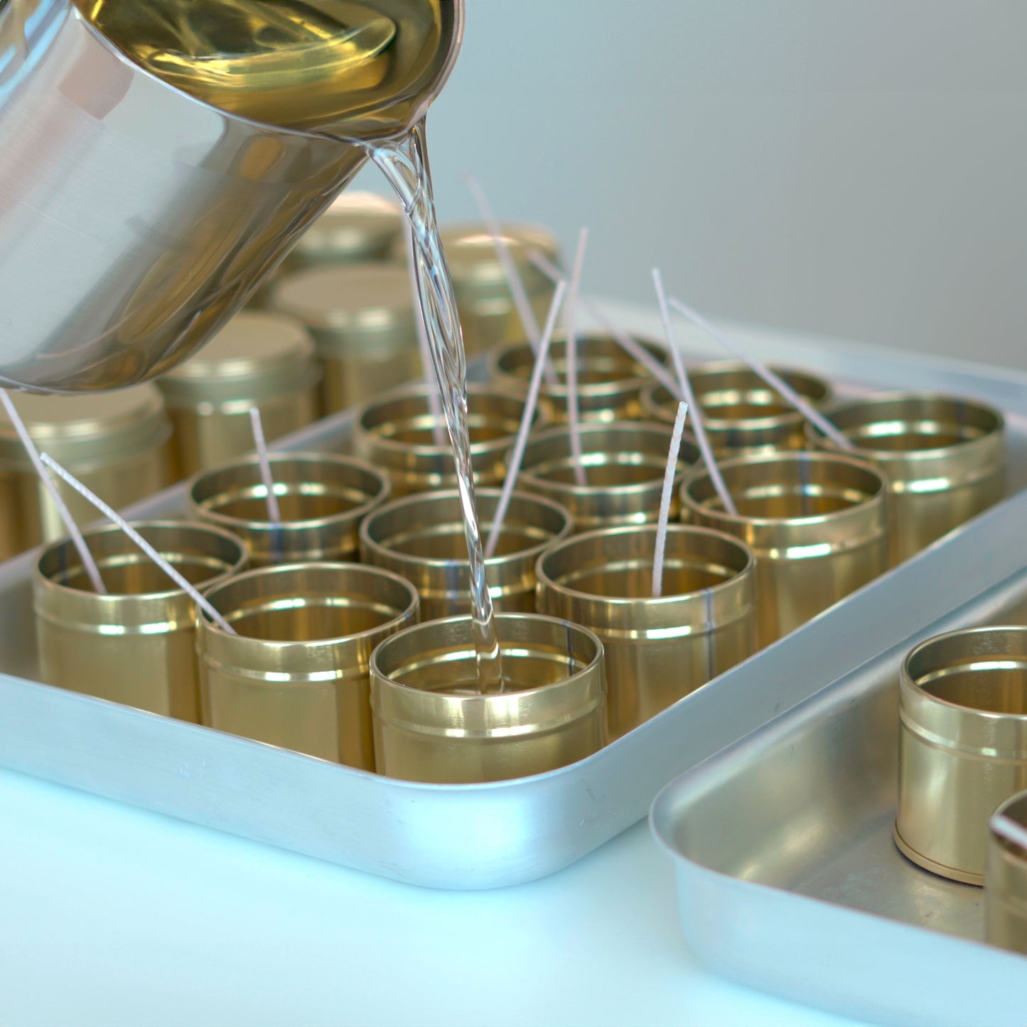 Tray filled with empty tins being filled with hot wax, capturing the process of hand-pouring Kalmyen candles. The warm glow of melted wax adds to the visual appeal of the scene.